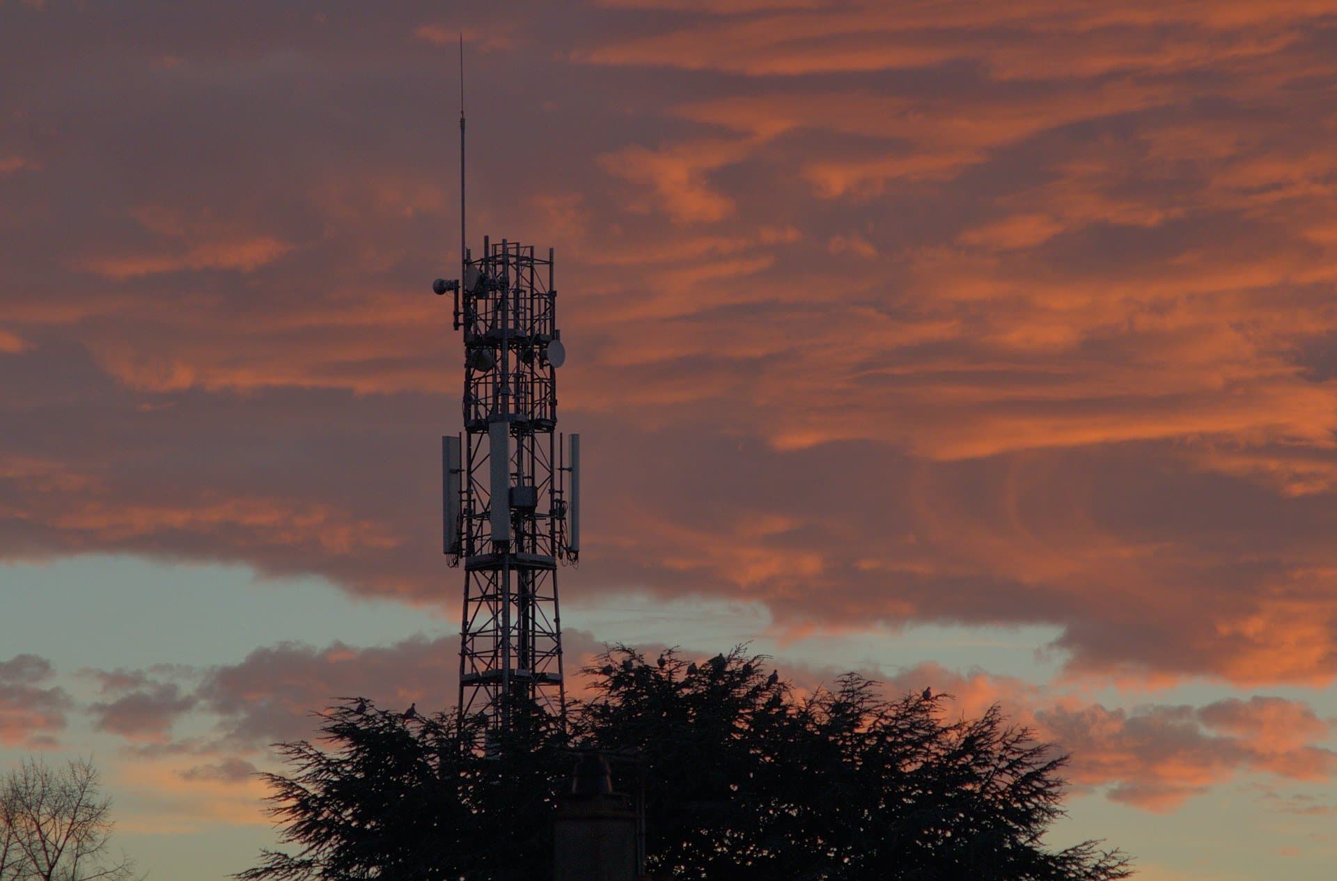 Telecommunications tower silhouetted against a dramatic sunset sky
